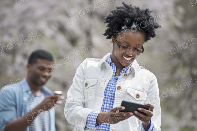 Outdoors in the city in spring. An urban lifestyle. A man and woman both checking…