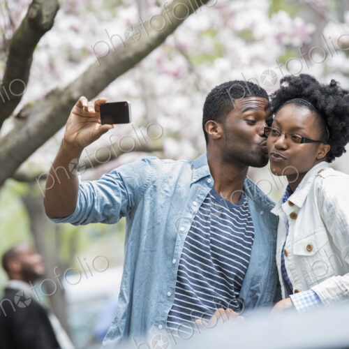 Outdoors in the city in spring. An urban lifestyle. A man kissing a woman and taking a… Outdoors in the city in spring. An urban lifestyle. A man kissing a woman and taking a…