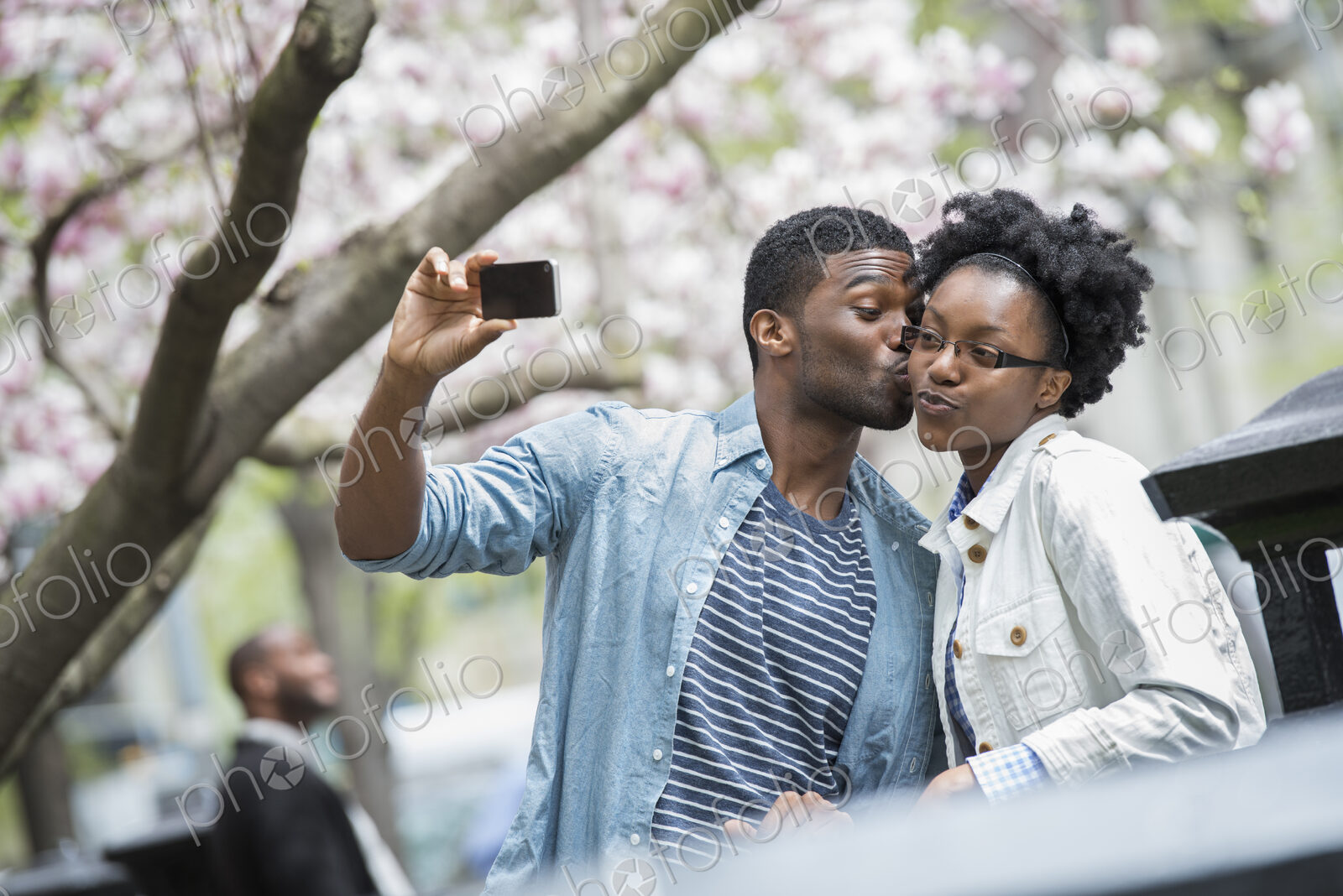 Outdoors in the city in spring. An urban lifestyle. A man kissing a woman and taking a…