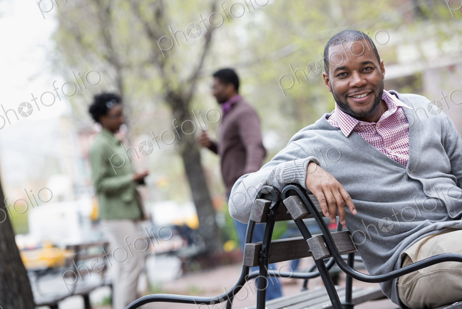 Outdoors in the city in spring. An urban lifestyle. A man seated on a bench, with two…