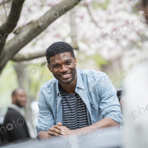 Outdoors in the city in spring. An urban lifestyle. A man sitting at a table smiling.…
