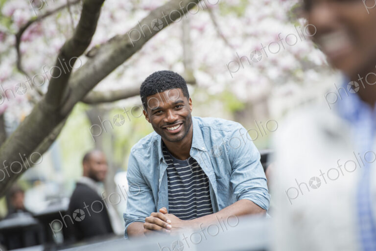 Outdoors in the city in spring. An urban lifestyle. A man sitting at a table smiling.…