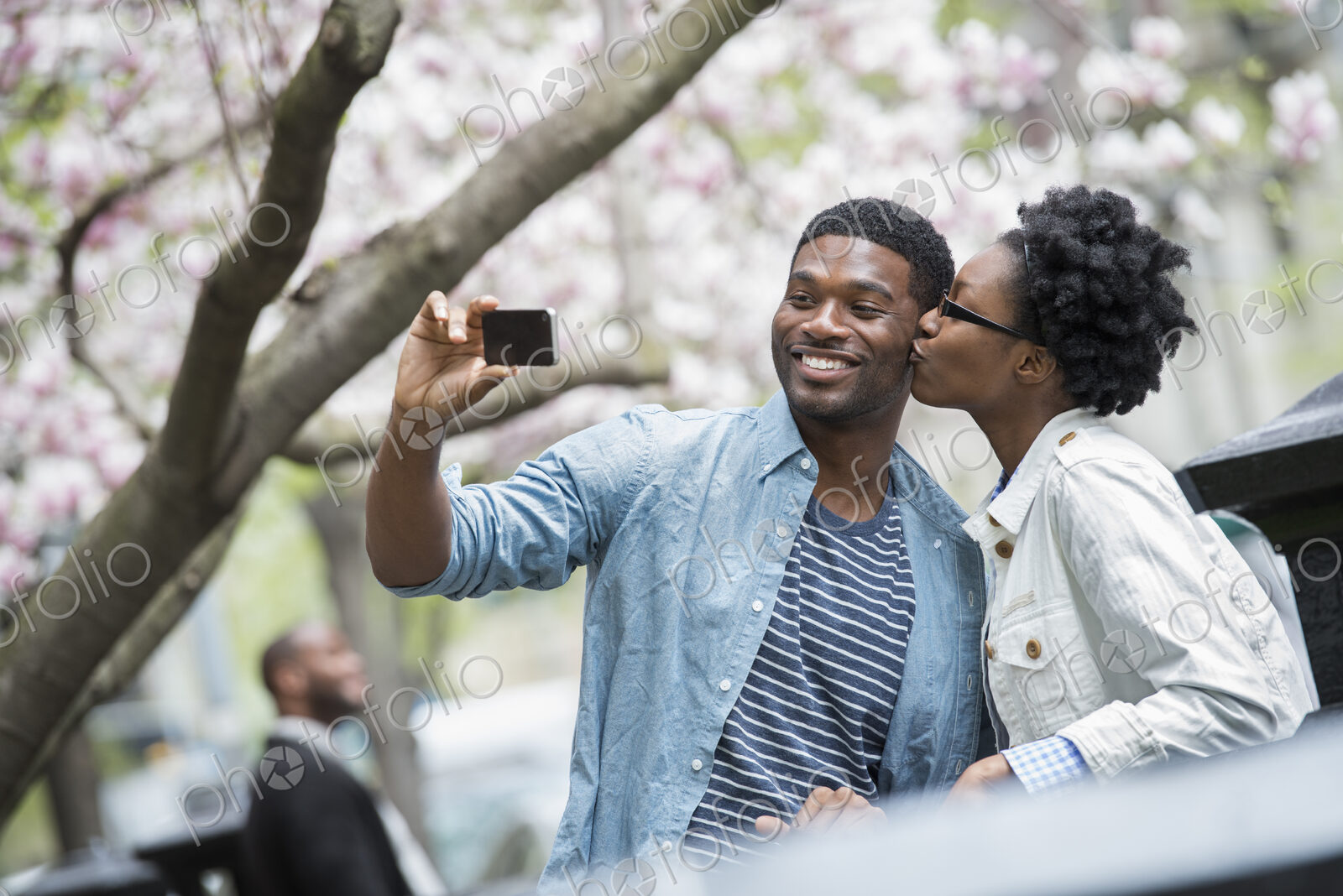 Outdoors in the city in spring. An urban lifestyle. A woman kissing a man and taking a…