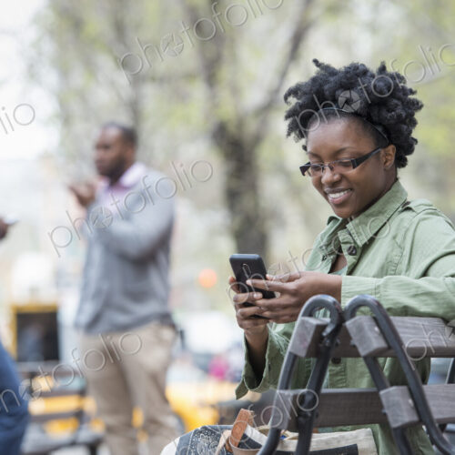 Outdoors in the city in spring. An urban lifestyle. A woman on a bench checking her… Outdoors in the city in spring. An urban lifestyle. A woman on a bench checking her…
