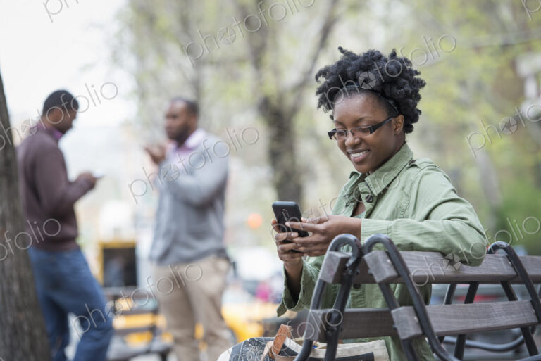 Outdoors in the city in spring. An urban lifestyle. A woman on a bench checking her…
