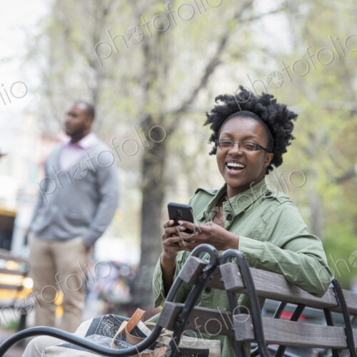 Outdoors in the city in spring. An urban lifestyle. A woman on a bench checking her… Outdoors in the city in spring. An urban lifestyle. A woman on a bench checking her…