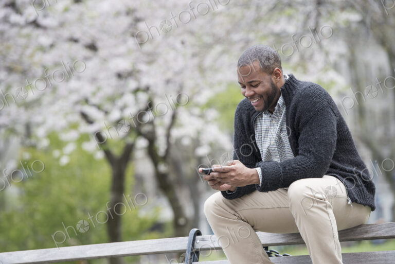 Outdoors in the city in spring. An urban lifestyle. A young man checking his phone and…