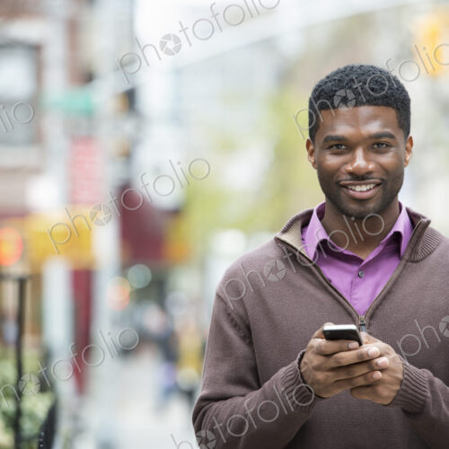 Outdoors in the city in spring. An urban lifestyle. A young man holding his phone, and…