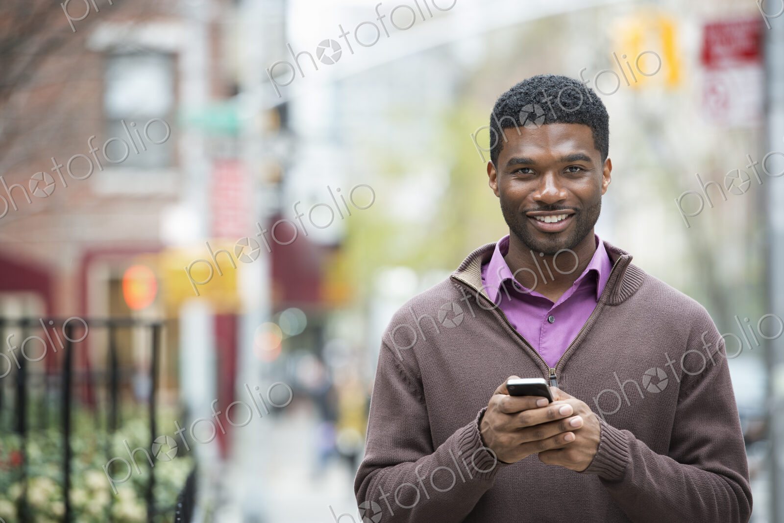 Outdoors in the city in spring. An urban lifestyle. A young man holding his phone, and…
