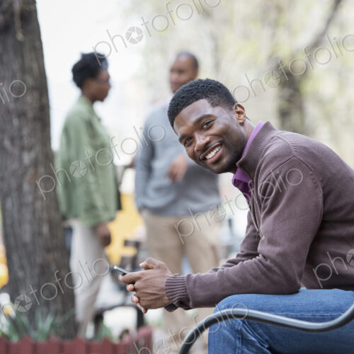 Outdoors in the city in spring. An urban lifestyle. A young man on a bench, and a… Outdoors in the city in spring. An urban lifestyle. A young man on a bench, and a…