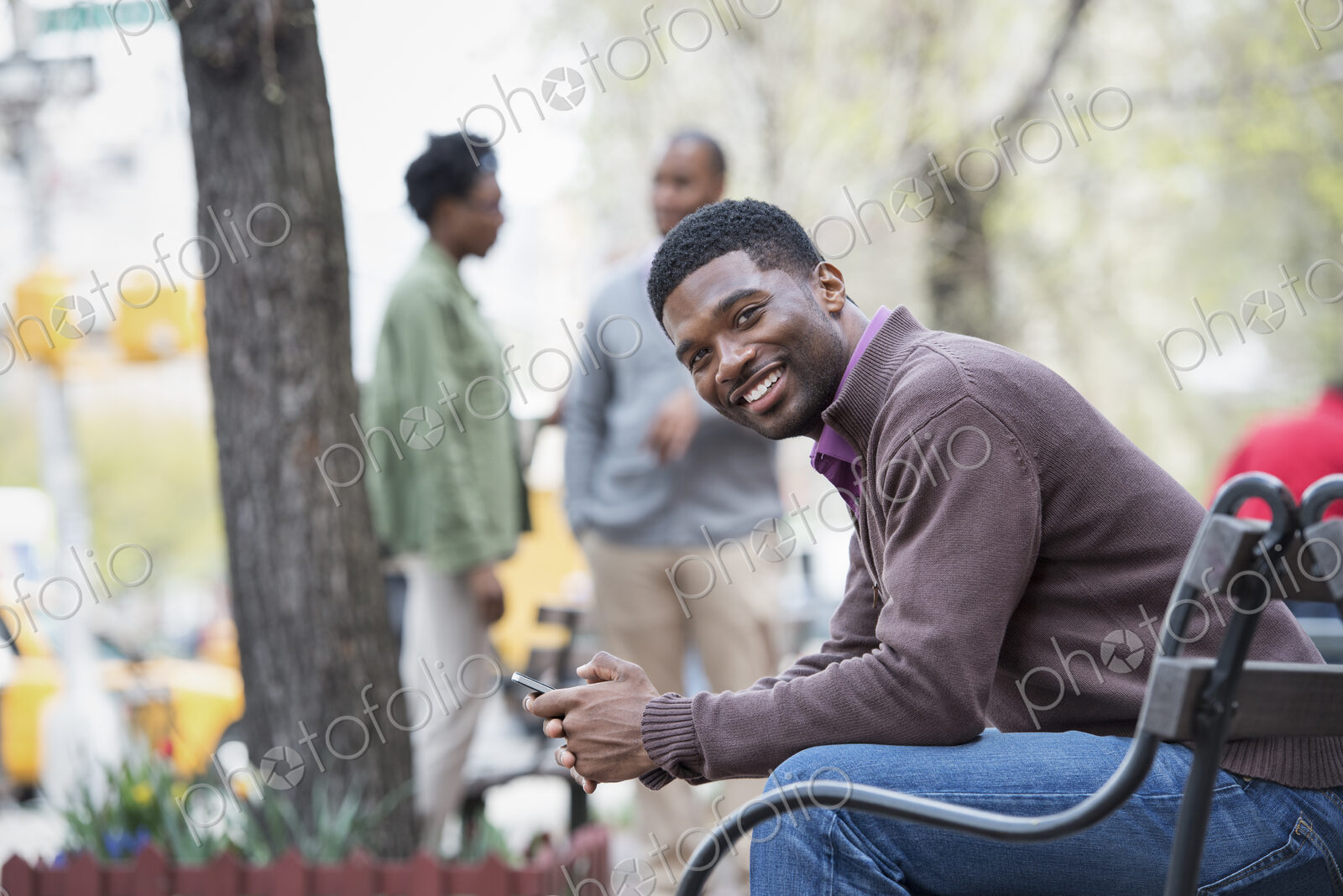 Outdoors in the city in spring. An urban lifestyle. A young man on a bench, and a…