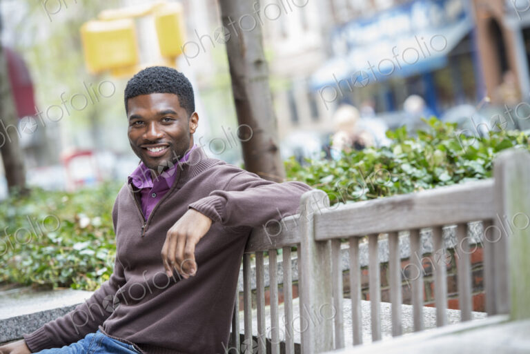 Outdoors in the city in spring. An urban lifestyle. A young man seated on a bench.
