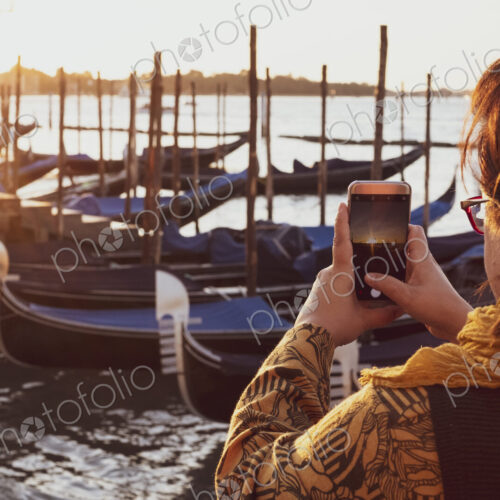 Over the shoulder view of woman taking picture of gondolas moored in the Canale Grande… Over the shoulder view of woman taking picture of gondolas moored in the Canale Grande…