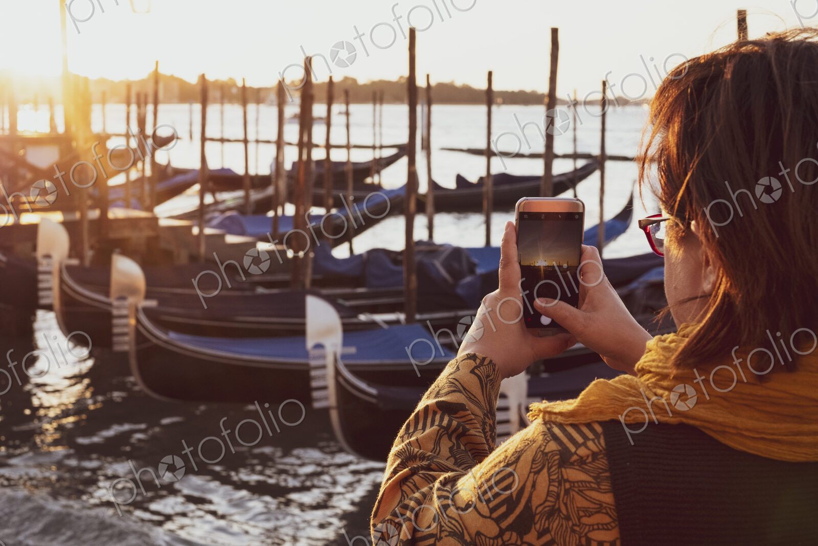 Over the shoulder view of woman taking picture of gondolas moored in the Canale Grande…