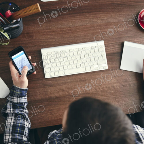 Overhead view of a man seated at a desk using a mobile phone.