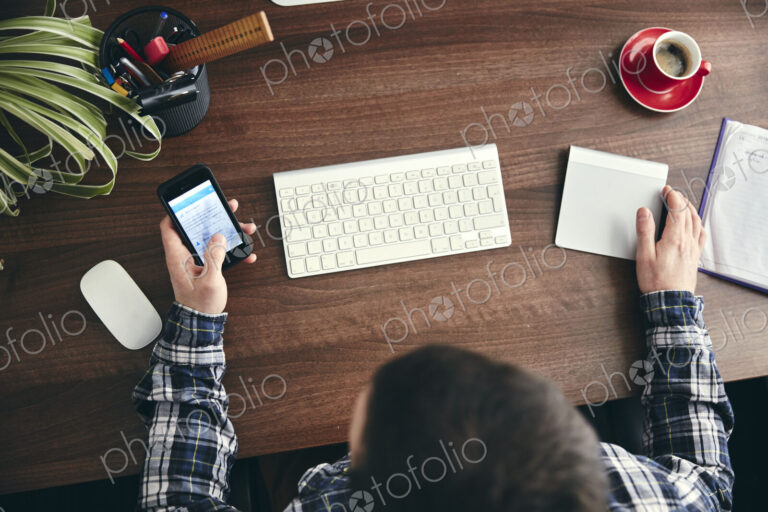 Overhead view of a man seated at a desk using a mobile phone.