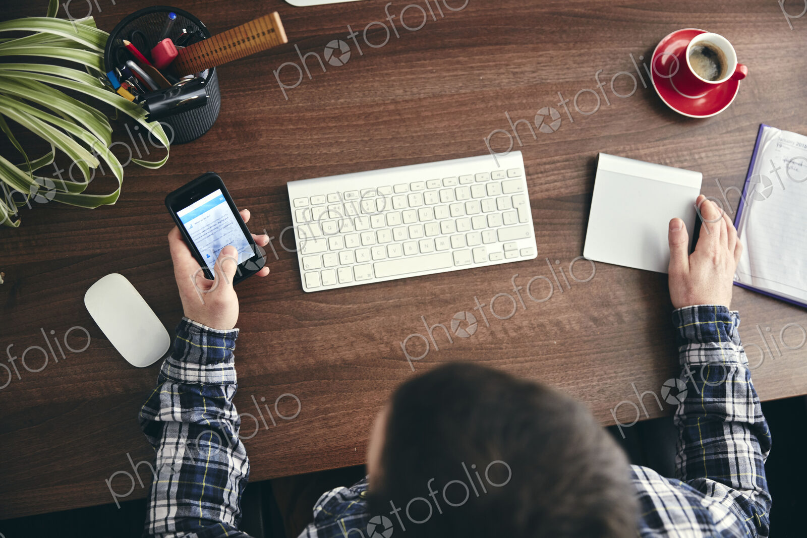 Overhead view of a man seated at a desk using a mobile phone.