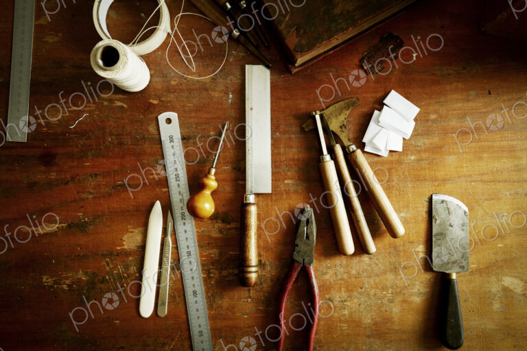 Overhead view of a workbench with hand tools for bookbinding.