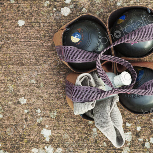 Overhead view of four wooden lawn bowls in a ball carrier with a cloth to clean them. Overhead view of four wooden lawn bowls in a ball carrier with a cloth to clean them.