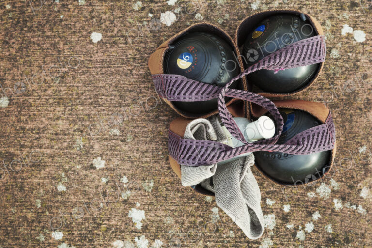 Overhead view of four wooden lawn bowls in a ball carrier with a cloth to clean them.