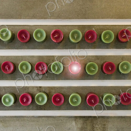 Overhead view of red and green candles lined up, one lit.