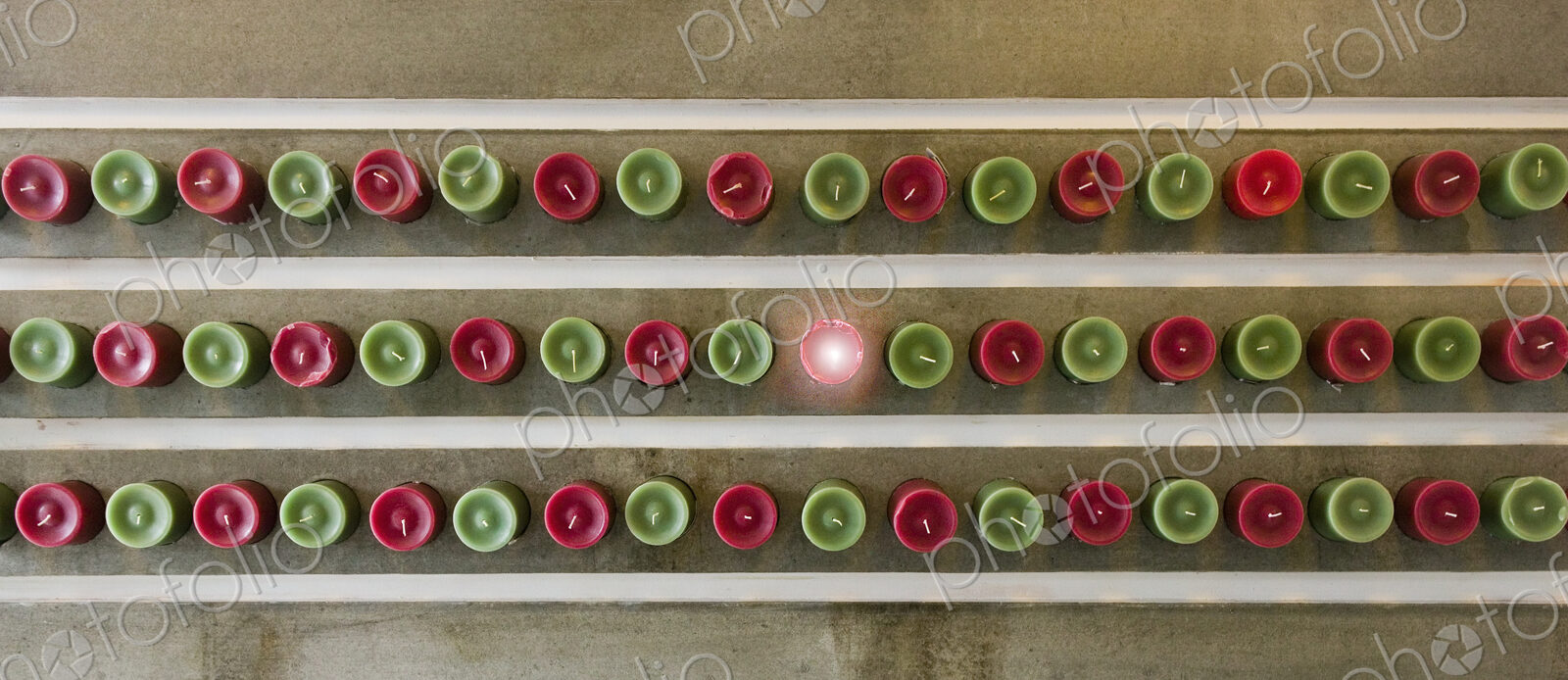 Overhead view of red and green candles lined up, one lit.
