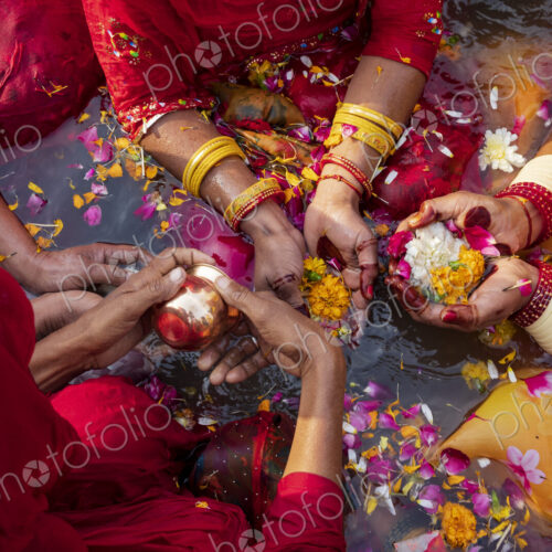 Overhead view of three women wearing bracelets, holding flowers and petals in their…