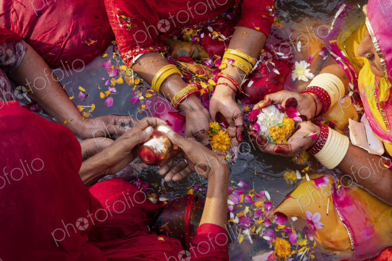 Overhead view of three women wearing bracelets, holding flowers and petals in their…