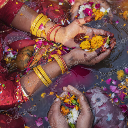 Overhead view of three women wearing bracelets, holding flowers and petals in their…