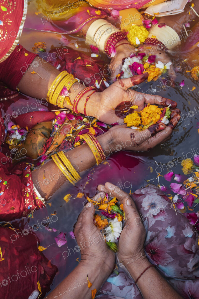 Overhead view of three women wearing bracelets, holding flowers and petals in their…