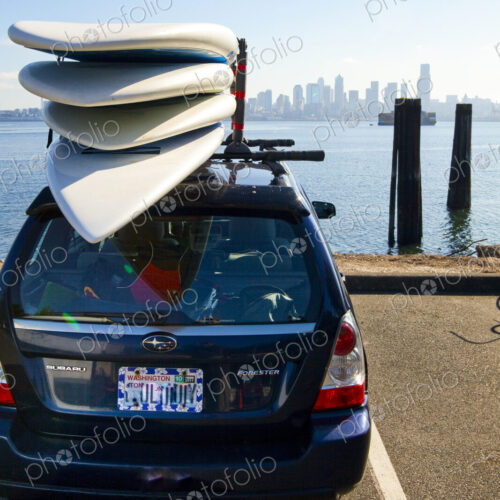 Paddle boards on top of a car parked with view of downtown Seattle and the water. Paddle boards on top of a car parked with view of downtown Seattle and the water.