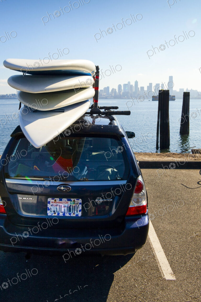 Paddle boards on top of a car parked with view of downtown Seattle and the water.