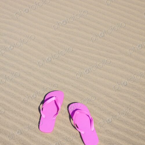 Pair of bright pink flip flops resting on smooth, rippled sand under the sun.