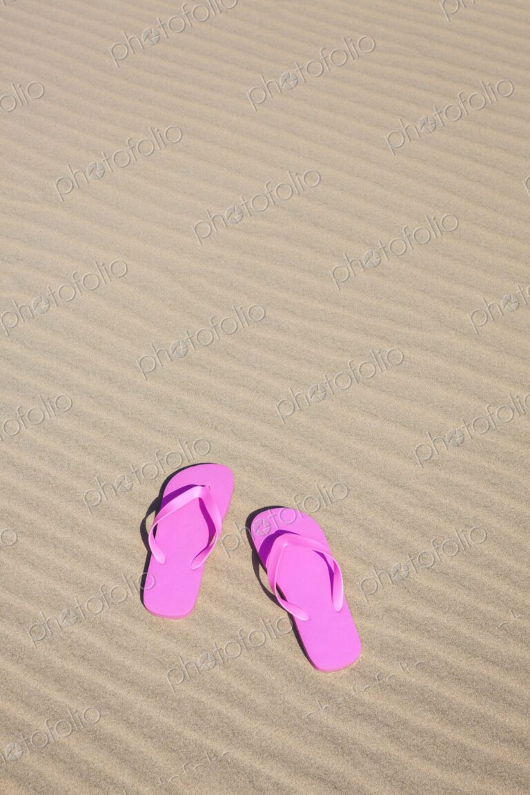 Pair of bright pink flip flops resting on smooth, rippled sand under the sun.