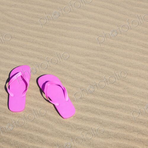Pair of bright pink flip flops resting on smooth, rippled sand under the sun. Pair of bright pink flip flops resting on smooth, rippled sand under the sun.