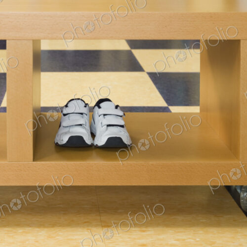 Pair of child's trainers in rolling storage crate on tiled floor.