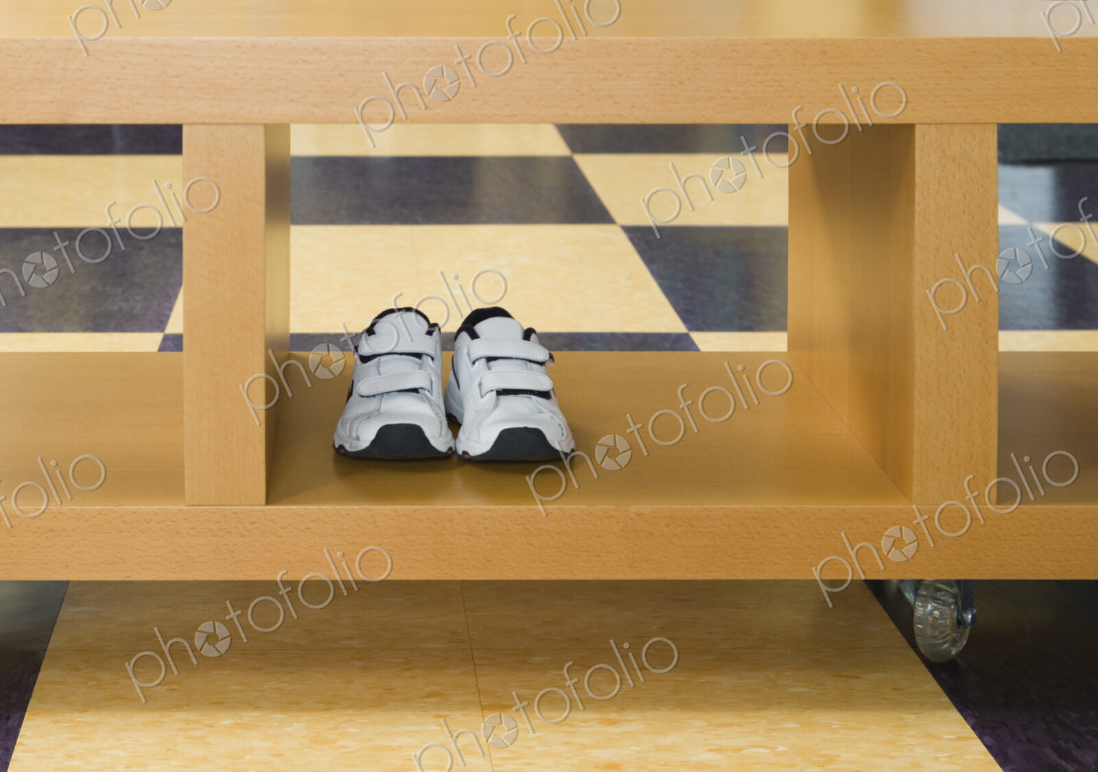 Pair of child’s trainers in rolling storage crate on tiled floor.
