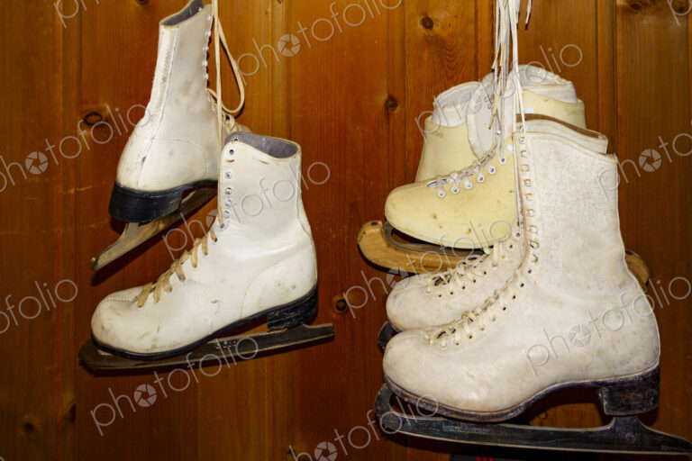 Pairs of ice skates hanging up in a room.