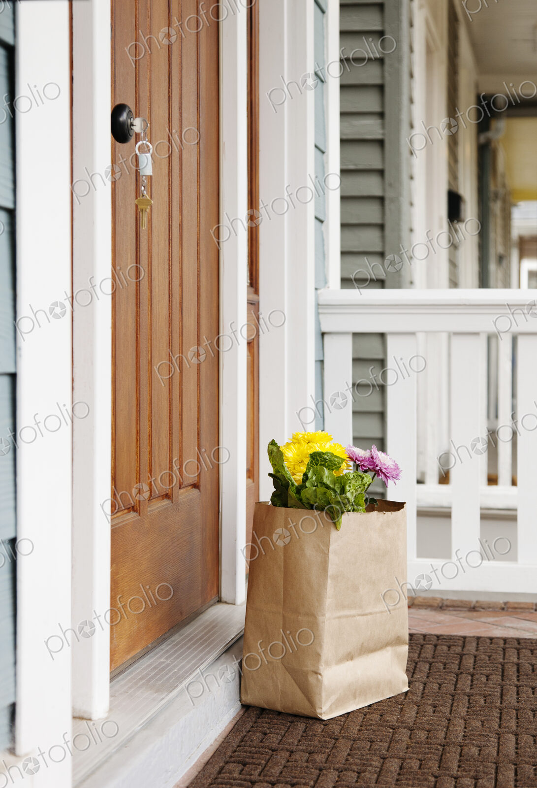 Paper bag with flowers on a porch in front of door.