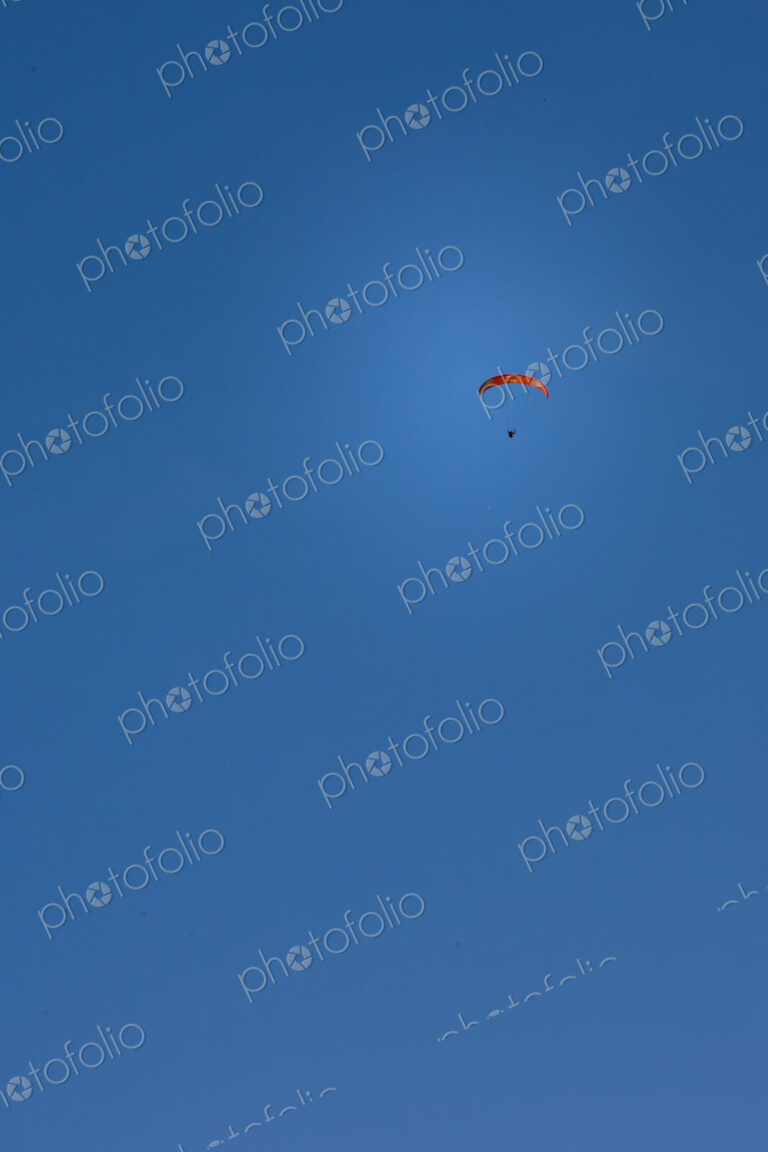 Paraglider above Yakima Canyon with a colourful canopy floating in a blue sky.