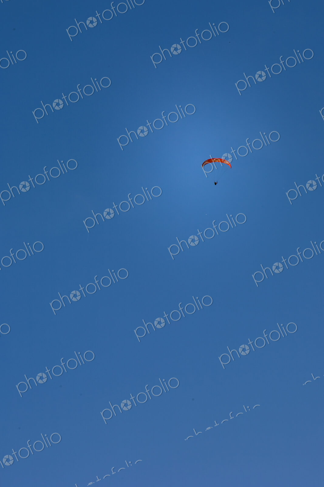 Paraglider above Yakima Canyon with a colourful canopy floating in a blue sky.