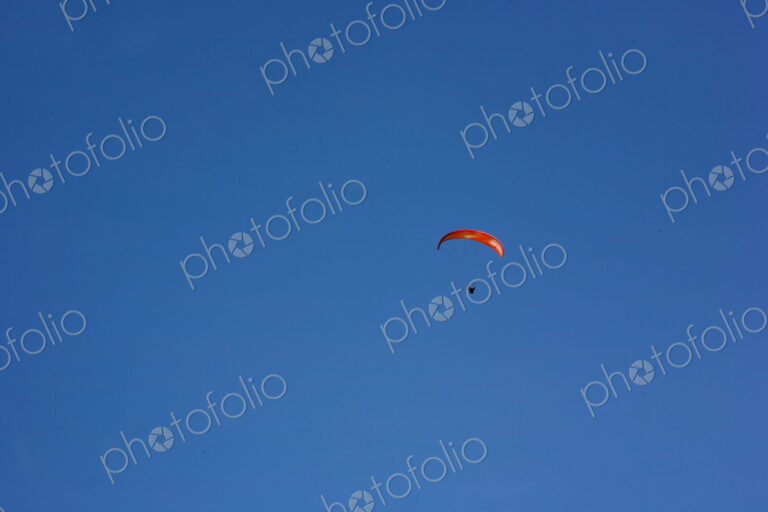 Paraglider above Yakima Canyon with a colourful canopy floating in a blue sky.