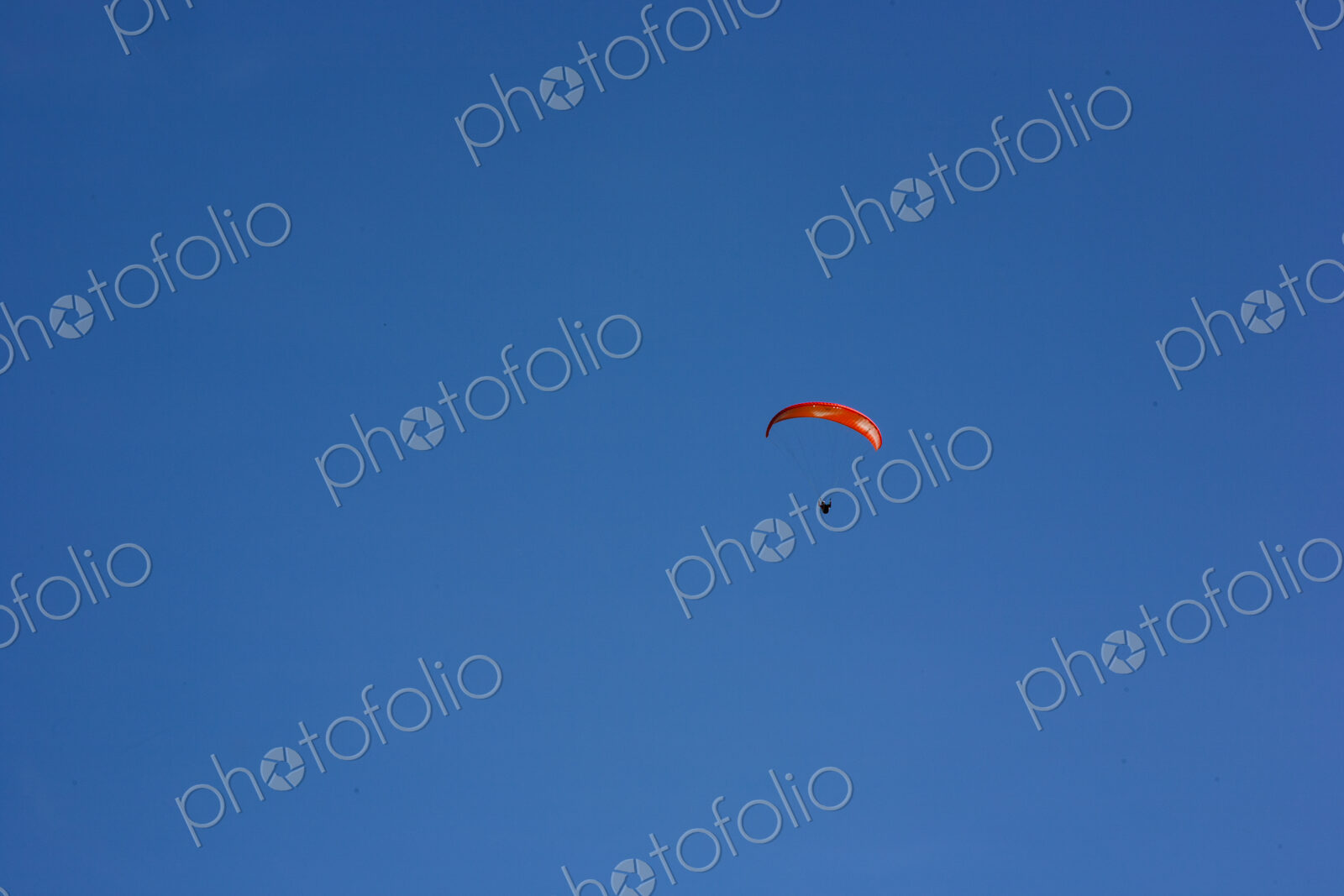Paraglider above Yakima Canyon with a colourful canopy floating in a blue sky.