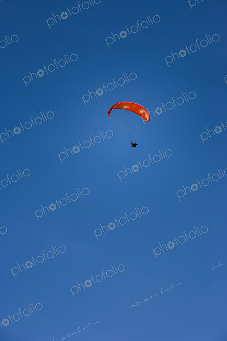 Paraglider above Yakima Canyon with a colourful canopy floating in a blue sky.