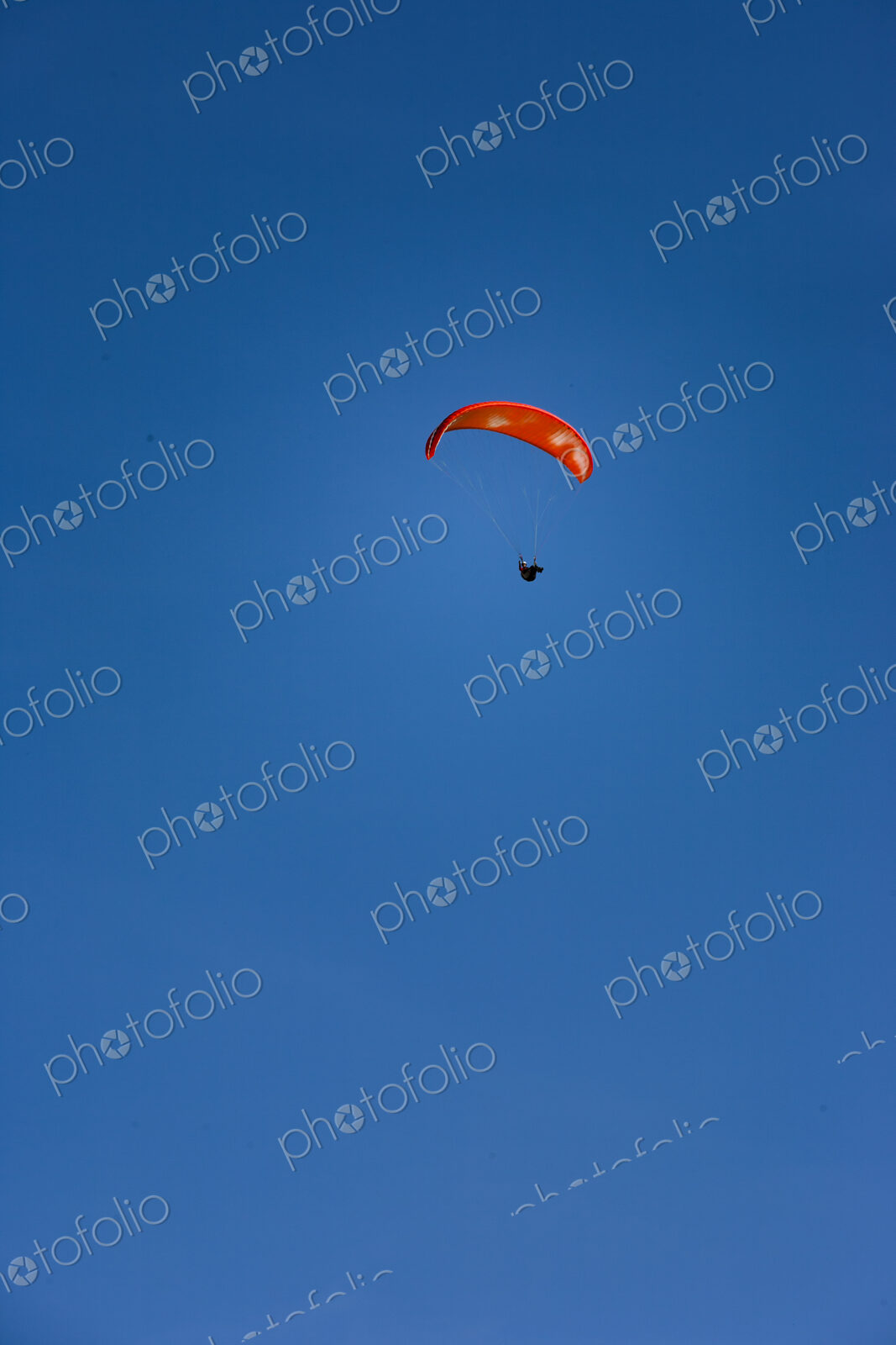 Paraglider above Yakima Canyon with a colourful canopy floating in a blue sky.