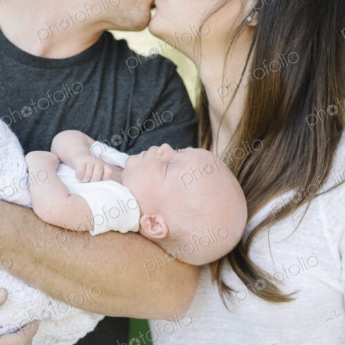 Parents holding a small baby and kissing, a group portrait. Parents holding a small baby and kissing, a group portrait.