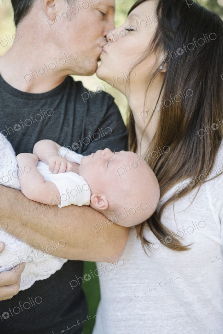 Parents holding a small baby and kissing, a group portrait.