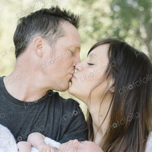 Parents holding a small baby and kissing, a group portrait. Parents holding a small baby and kissing, a group portrait.