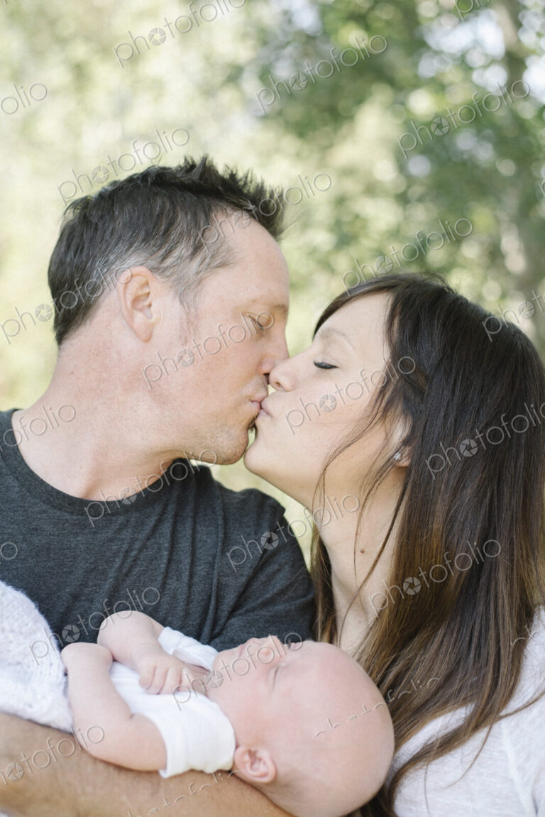 Parents holding a small baby and kissing, a group portrait.