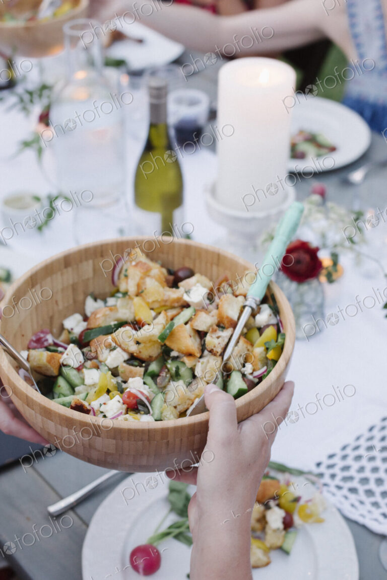 People around a table at a garden party, a bowl of salad.